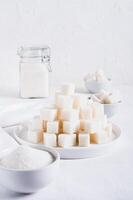 Lump sugar on a plate and granulated sugar in a bowl and jar on the table vertical view photo