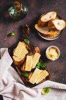 Fried bread toasts with cheese and basil on a board on the table top and vertical view photo