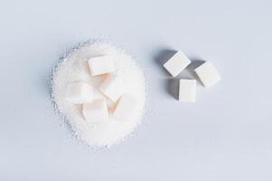 Lump sugar on a pile of granulated sugar and next to it on a blue background, top view photo