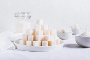Lump sugar on a plate and granulated sugar in a bowl and jar on the table photo