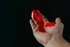 AID red ribbon in hand on gray dot background, symbol of the fight against HIV, AIDS and cancer. Concept of helping those in need, close-up photo. photo