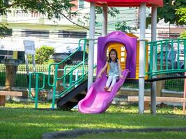 Cute girl having fun on a colorful slide in an outdoor park. Children playing in the playground during summer vacation. photo