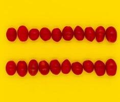 Red cherry tomatoes arranged in parallel lines on a bright yellow background. photo