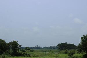 A wide, green landscape stretches under a hazy blue sky photo