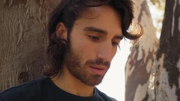 Long Hair Man With Eye Tic Plays Nerd On The Phone In Nature Under Tree video