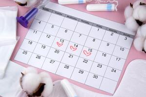 Women's menstrual pads, tampons, female menstruation calendar and alarm clock on a pink background. photo