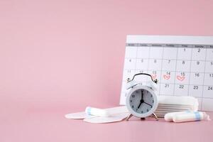 Women's menstrual pads, tampons, female menstruation calendar and alarm clock on a pink background. photo