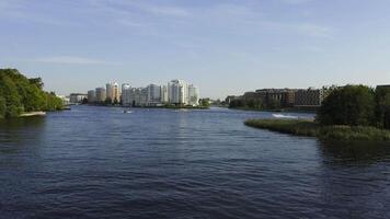 A panoramic view of modern residential buildings along a riverbank in Saint Petersburg. The lush green trees on the opposite shore contrast with the contemporary architecture, creating a peaceful video