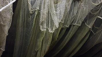 A detailed close-up of weathered fishing nets draped over each other, with a white rope intertwined above. The texture of the nets shows signs of use, adding to the rustic maritime scene. Captured at video