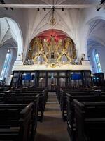 A detailed low-angle view of the historic pipe organ in Konigsberg Cathedral. The baroque design features intricate gold ornamentation and angelic sculptures, framed by soaring gothic arches and photo