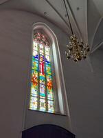A pair of towering stained glass windows inside Konigsberg Cathedral in Kaliningrad, showcasing vibrant religious scenes and intricate geometric designs. The colorful panels depict various figures and photo