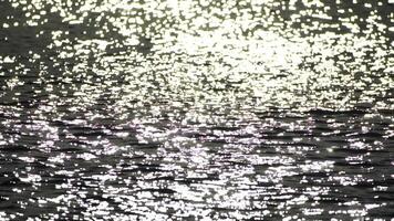 Abstract shining sun reflections on blue surface of sea waves. Bokeh sun glare reflected in water surface. The shimmering small sea waves in sun. Sea on sunny day. Natural bokeh texture. Slow motion video