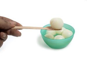 Close-up of hand taking traditional Indian dessert rasgulla from green bowl with wooden spoon photo