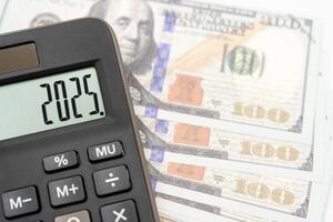 US Dollar banknotes, calculator and forecast for finances in 2025. Money, Budget, tax, investment, financial, savings and New Year Resolution concepts. calculator with 2025 numbers. photo