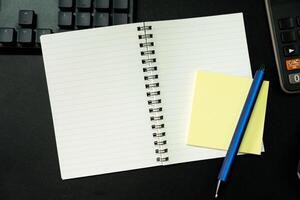 Top view of notebook. Blank paper notepad on office desk table with keyboard and other supplies. Blank notebook page for input the text. copy space, flat lay. photo