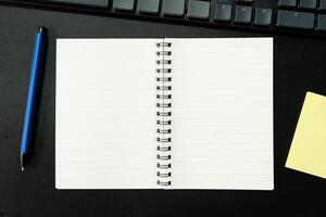 Top view of notebook. Blank paper notepad on office desk table with keyboard and other supplies. Blank notebook page for input the text. copy space, flat lay. photo