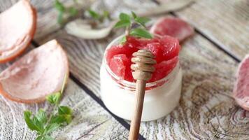 homemade sweet yogurt in a glass jar with pieces of red ripe grapefruit and honey, on a wooden table video