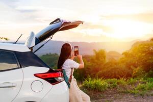 Young woman traveler sitting with car watching a beautiful sunrise over the mountain while traveling road trip on vacation, Travel concept photo