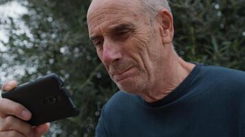 Elderly Man Fumes At Players While Watching A Game On The Phone Under A Tree video