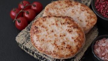 Grilled chicken burger cutlet with salt, spices and herbs on a dark concrete background video