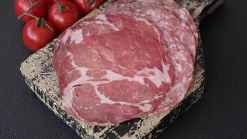 Antipasto jamon, prosciutto, sausage, sliced with tomatoes, salt and spices on a dark concrete background video