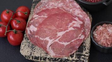 Antipasto jamon, prosciutto, sausage, sliced with tomatoes, salt and spices on a dark concrete background video
