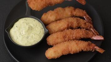 Hot crispy shrimp breaded with salt and spices with white sauce on a dark concrete background video
