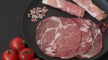 Antipasto jamon, prosciutto, sausage, sliced with tomatoes, salt and spices on a dark concrete background video
