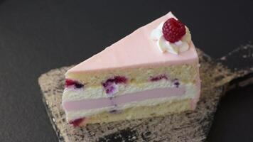 Piece of sweet cake with pink cream with raspberry flavor, with shortbread, cheesecake on a dark concrete background video