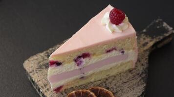 Piece of sweet cake with pink cream with raspberry flavor, with shortbread, cheesecake on a dark concrete background video