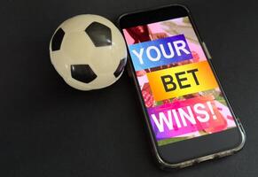 Smartphone with gambling mobile application and soccer ball close-up. Sport and betting concept photo