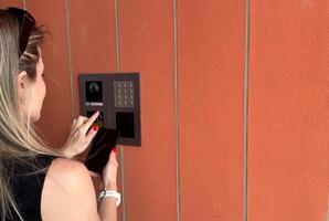 female entering secret key code for getting access and passing building using application on mobile phone, woman pressing buttons on control panel for disarming smart home system photo