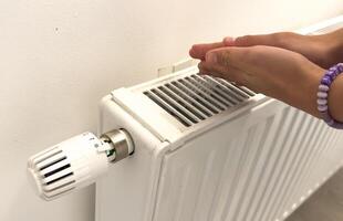 Closeup of woman warming her hands on the heater at home during cold winter days, top view. Female getting warm up her arms over radiator. Concept of heating season, cold weather. photo