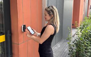 Happy woman ringing on doorbell at building entrance. Using intercom. photo