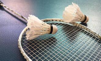 Cream white badminton shuttlecock and racket with neon light shading on floor in indoor badminton court, copy space, soft and selective focus. photo