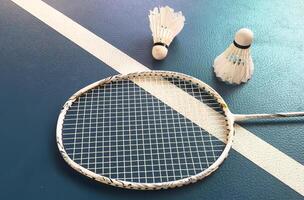 Cream white badminton shuttlecock and racket with neon light shading on floor in indoor badminton court, copy space, soft and selective focus. photo