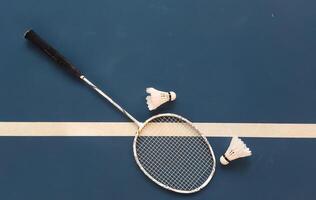 Cream white badminton shuttlecock and racket with neon light shading on dark floor in indoor badminton court, copy space, soft and selective focus. photo