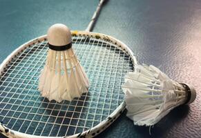 Cream white badminton shuttlecock and racket with neon light shading on dark floor in indoor badminton court, copy space, soft and selective focus. photo