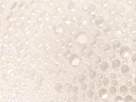 A close-up view of numerous water droplets on a transparent surface, creating a soft, dreamy texture with a white and pastel background. photo