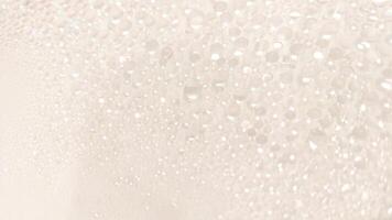 A close-up view of numerous water droplets on a transparent surface, creating a soft, dreamy texture with a white and pastel background. photo