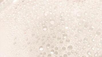 A close-up view of numerous water droplets on a transparent surface, creating a soft, dreamy texture with a white and pastel background. photo