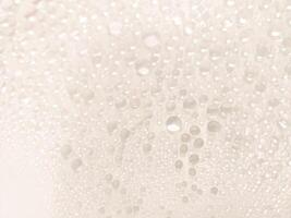 A close-up view of numerous water droplets on a transparent surface, creating a soft, dreamy texture with a white and pastel background. photo