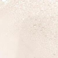 A close-up view of numerous water droplets on a transparent surface, creating a soft, dreamy texture with a white and pastel background. photo