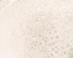 A close-up view of numerous water droplets on a transparent surface, creating a soft, dreamy texture with a white and pastel background. photo