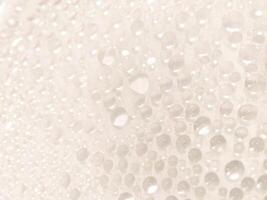 A close-up view of numerous water droplets on a transparent surface, creating a soft, dreamy texture with a white and pastel background. photo