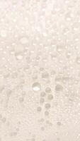 A close-up view of numerous water droplets on a transparent surface, creating a soft, dreamy texture with a white and pastel background. photo