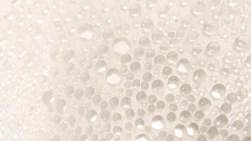 A close-up view of numerous water droplets on a transparent surface, creating a soft, dreamy texture with a white and pastel background. photo