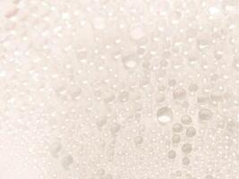 A close-up view of numerous water droplets on a transparent surface, creating a soft, dreamy texture with a white and pastel background. photo