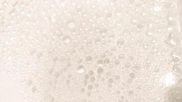 A close-up view of numerous water droplets on a transparent surface, creating a soft, dreamy texture with a white and pastel background. photo