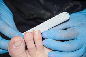 The pedicure master grinds the toenails of clients with a nail file, polishes polishing the nail plate with a buff, High quality photo